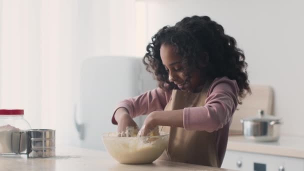 Linda niña afroamericana con la cara sucia amasando masa en un tazón de cristal y sonriendo, cocinando hornear en la cocina — Vídeo de stock