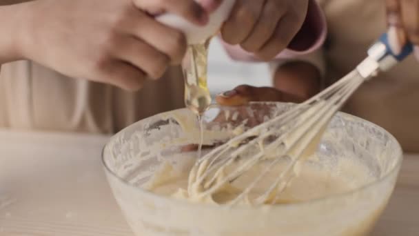 Proceso de cocción. Primer plano de niña negra añadiendo huevo a la masa, madre mezclándolo, horneando en la cocina juntos — Vídeo de stock