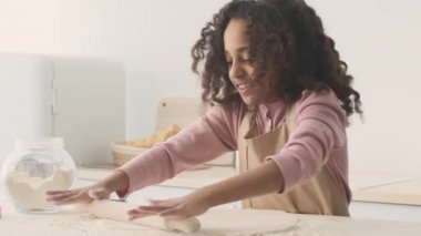 Afro-Amerikalı neşeli kızın çiğ hamuru tokayla saran portresini kapat, mutfakta ev yapımı kurabiyeler hazırla.