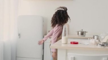 Sevimli mutlu Afrikalı Amerikalı kız annesine koşuyor ve ona mutfakta hamur işlerinde yardım ediyor.