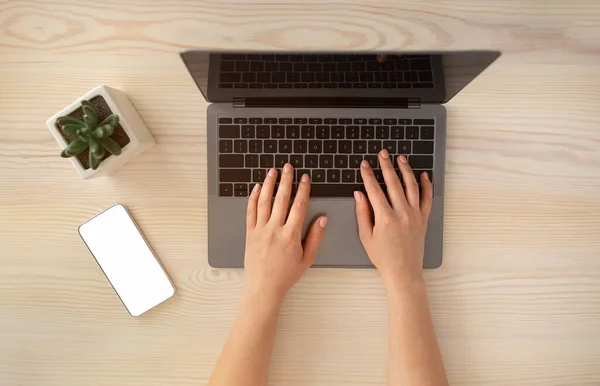 Kvinnelige hender som skriver på et laptop-tastatur og bruker smarttelefon med tom skjerm, sittende på trebord, flott utsikt – stockfoto