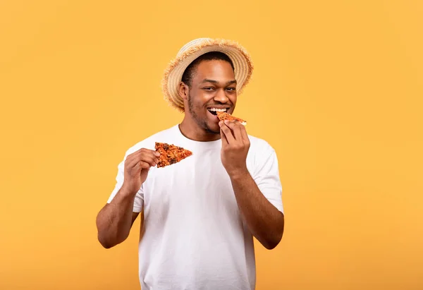 Cara afro-americano faminto em roupa de verão na moda comer pizza, tendo lanche no fundo do estúdio amarelo — Fotografia de Stock