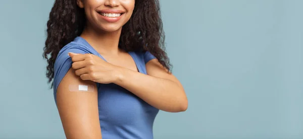 Erfolgreiche Covid-19-Impfung. Glückliche, nicht wiedererkennbare schwarze Frau zeigt Arm mit Gips, blauer Hintergrund, freier Raum — Stockfoto