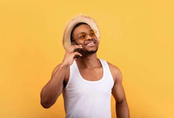 Positiv svart man i sommar slitage ringer på smartphone, har trevliga samtal över gul studio bakgrund — Stockfoto