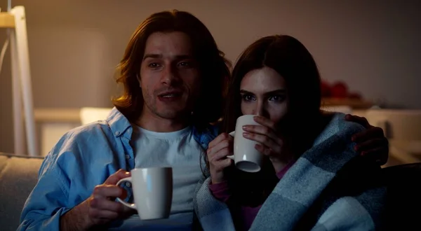 Porträtt av lyckliga par förälskade tittar på tv tillsammans hemma, omfamnar på dricka te, kvinna insvept i rutig — Stockfoto