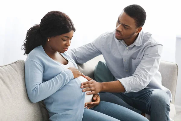 Mulher grávida com dores de parto, sentada com o marido no sofá — Fotografia de Stock