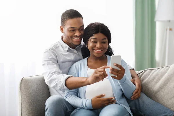 Loving black expecting parents shopping online, using smartphone — 스톡 사진