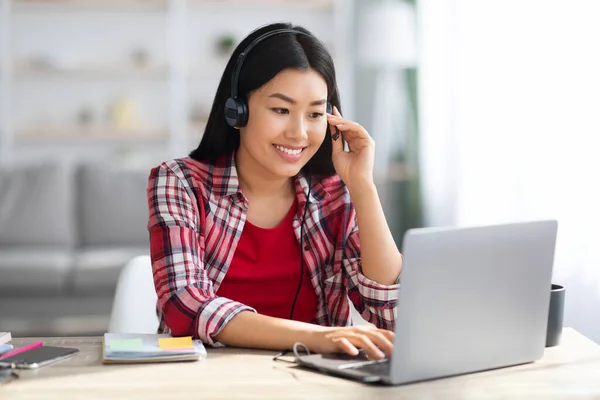 Εκμάθηση εξ αποστάσεως. Χαρούμενη Ασιάτισσα γυναίκα σε ακουστικά που σπουδάζει με φορητό υπολογιστή στο σπίτι — Φωτογραφία Αρχείου