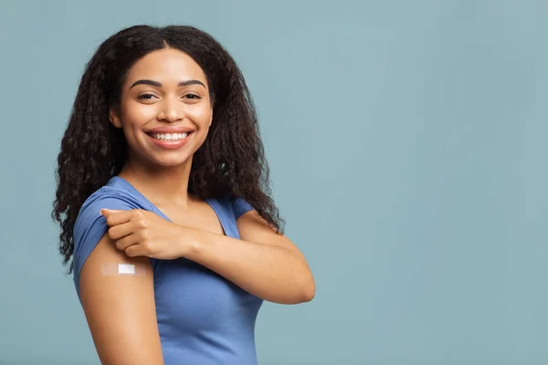 Megvan a kovid-19 vakcinám. Boldog afro-amerikai hölgy mutatja oltott kar után antivirális injekció, kék háttér — Stock Fotó