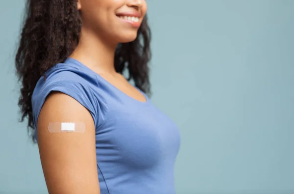 Conceito de vacinação. Senhora negra irreconhecível feliz mostrando braço vacinado com gesso, fundo azul, espaço livre — Fotografia de Stock