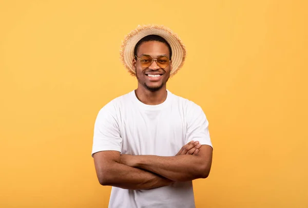 O verão chegou. Retrato do jovem negro sorridente em camiseta branca, chapéu de palha e óculos de sol posando com braços cruzados — Fotografia de Stock