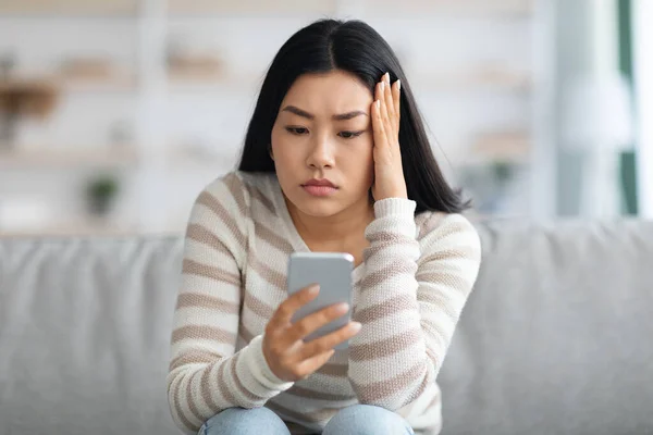 Brutte notizie. Sconvolto femminile asiatico che tiene lo smartphone, guardando lo schermo con preoccupazione — Foto Stock