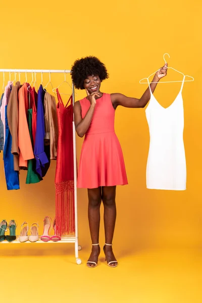 Afrikaans-Amerikaanse vrouw bij het winkelen Kiezen van kleding, Gele achtergrond, Verticaal — Stockfoto