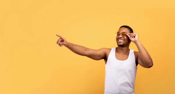 Sorridente ragazzo nero in abito estivo alla moda che punta lo spazio vuoto su sfondo giallo studio, panorama — Foto Stock