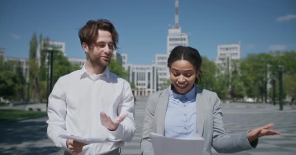 Projecto de negócio bem sucedido. Homem caucasiano e senhora americana africana andando ao ar livre com documento — Vídeo de Stock