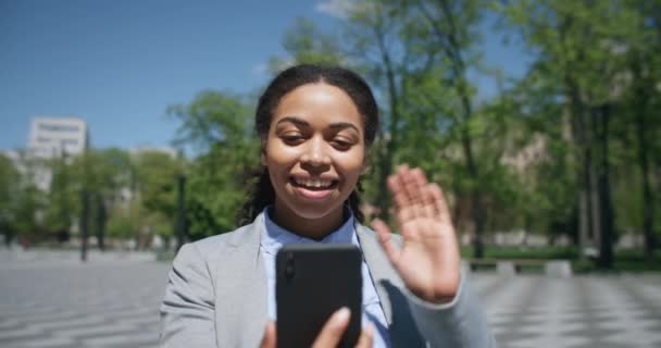 Positivo Africano americano empresária senhora acenando mão para smartphone, vídeo conversando com parceiros on-line no parque — Vídeo de Stock