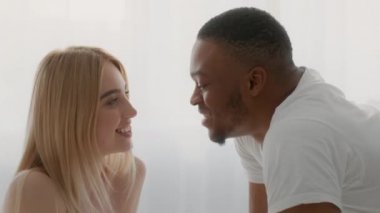 Çok ırklı mutlu çift birlikte güneşleniyor, siyah adam sevgili sarışın sevgilisinin kulağına hassas şeyler fısıldıyor.