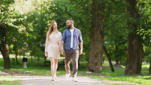 Нежная влюбленная пара, держащаяся за руки и идущая по дорожке в летнем парке, мужчина обнимает свою девушку — стоковое видео