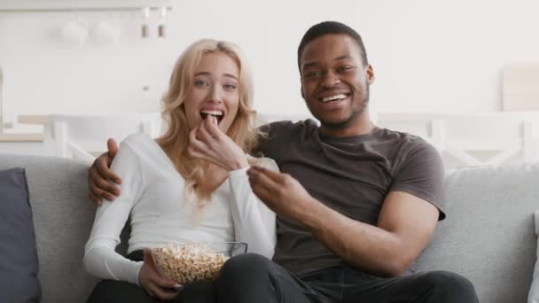Diverso casal rindo assistindo TV comendo pipoca em casa — Vídeo de Stock
