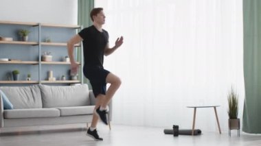 Evde kardiyo çalışması. Genç sporcu oturma odasında antrenman yapıyor, dizlerini pencereye dayayıp koşuyor.