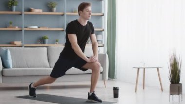 Erkekler için pilates. Genç sporcu evde esneme antrenmanı yapıyor, tek ayak üzerinde hamleler yapıyor.