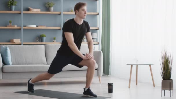 Pilates férfiaknak. Fiatal sportos srác gyakorolja nyújtás edzés otthon, csinál rugós tüdő gyakorlat az egyik lábán — Stock videók
