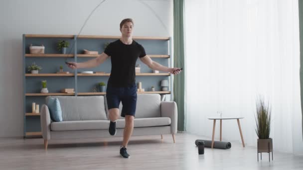 Träning hemma. Aktiv energisk idrottsman utför cardio träning med hopprep, utövar i vardagsrummet — Stockvideo