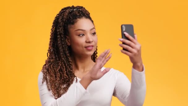 Joven mujer afroamericana con afro peinado video chat con amigos, saludando de la mano al teléfono inteligente y hablando — Vídeos de Stock