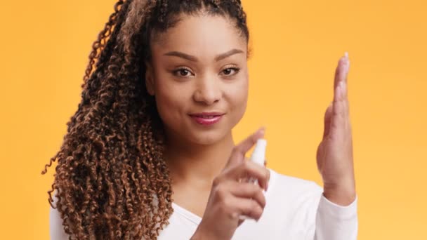 Mladý pozitivní africký Američan žena sprejování tekutý alkohol dezinfekci na dlani a usmívat se na kameru, oranžové pozadí — Stock video