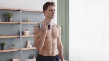 Çıplak gövdesi olan genç, konsantre olmuş kaslı adam halterleri kaldırıyor, evde kol kaslarını güçlendiriyor.