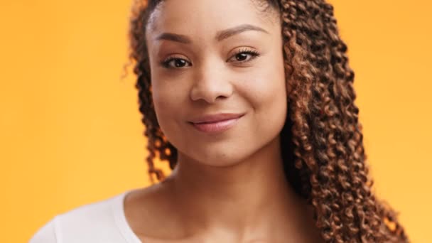 Primer plano retrato de juguetona dama afroamericana guiñando un ojo y sonriendo a la cámara, fondo de estudio naranja, cámara lenta — Vídeo de stock