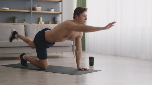 伸展训练。年轻的肌肉发达的男子，赤身裸体，抬起腿和手，四脚朝天地站在家里的地板上 — 图库视频影像