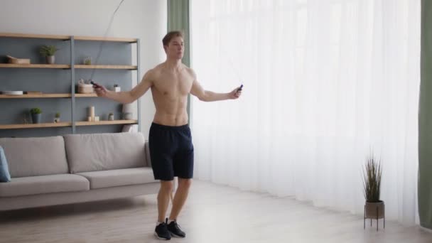 Young shirtless athlete with muscular torso exercising with jumping rope at home, tracking shot, slow motion — Stock Video