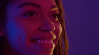 Yarı profil portresi, neon ışıklarıyla boş alana bakan, gülümseyen genç Afrikalı Amerikalı kadının portresi.