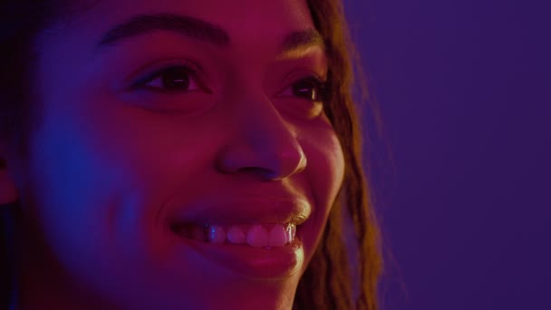 Félprofil portré fiatal pozitív afro-amerikai nő mosolyog, félrenéz szabad hely neon fények — Stock videók
