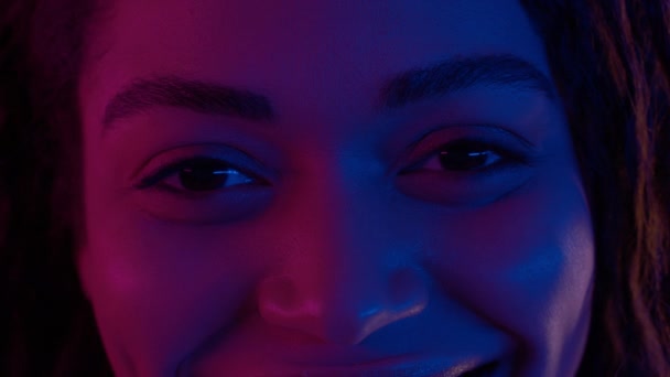 Neon lights shot of eyes of young happy african american woman looking to camera, red and purple illumination — Stock Video