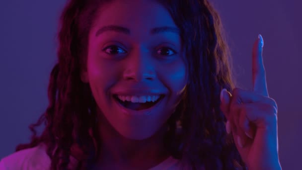 Creative thinking. Young african american lady pointing finger up and smiling, having great idea, posing in neon lights Video Clip