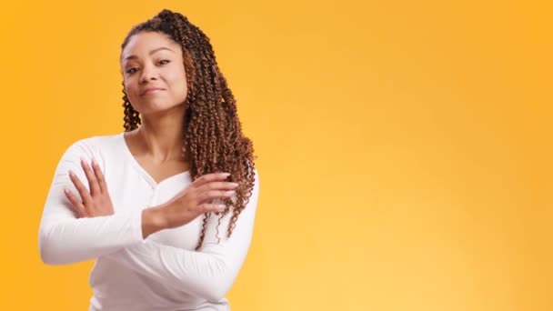 Jong vertrouwen Afrikaans amerikaanse vrouw kijken naar camera met gevouwen armen, oranje studio achtergrond met vrije ruimte — Stockvideo