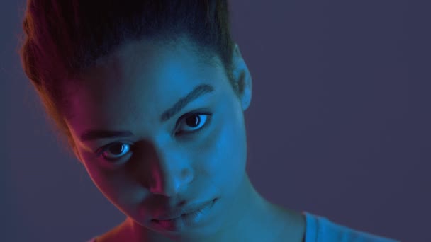 Jovem afro-americana sombria olhando sullenly para câmera, posando em luzes de néon fundo, close up retrato — Vídeo de Stock