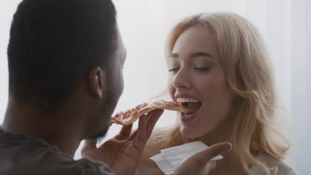 Diversa pareja comiendo pizza alimentándose unos a otros coqueteando en interiores — Vídeos de Stock