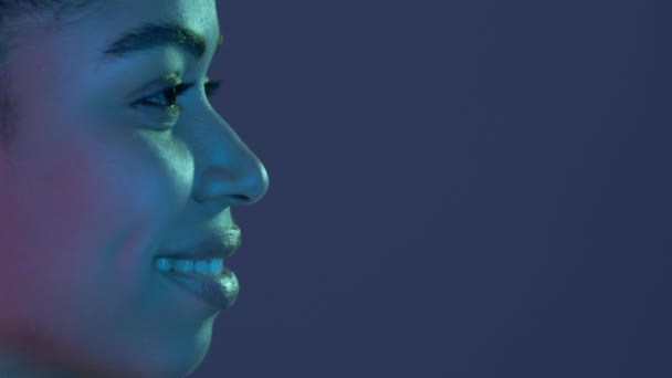 Afro-Amerikalı genç bir kadının profil portresi. Gülümsüyor ve mavi neon ışıklardaki boş alana bakıyor. — Stok video