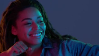 Gece kulübü eğlencesi. Neşeli Afro-Amerikan bayan dans ediyor, neon ışıklarda disko müziğinden hoşlanıyor, mavi stüdyo geçmişi var.