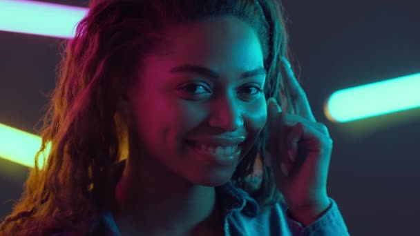 Usa la mente. Giovane donna afroamericana toccando dito la testa e sorridendo alla fotocamera, posa in lampade al neon luce — Video Stock