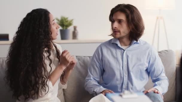 Jovens cônjuges emocionais conversando na consulta psicológica pessoal, discutindo e brigando no sofá no escritório — Vídeo de Stock