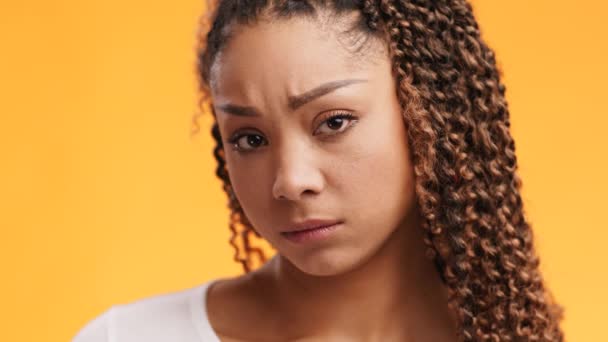 Młoda, zdenerwowana Afroamerykanka patrzy smutno w kamerę, czuje się zaniepokojona i obrażona, pomarańczowe tło studia — Wideo stockowe
