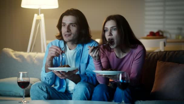 令人兴奋的电影。年轻男女在家里吃饭，晚上看电视，一起坐在沙发上 — 图库视频影像