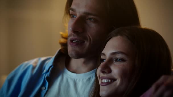 Feliz noite de família. Close up retrato de jovens cônjuges alegres abraçando e assistindo tv em casa juntos — Vídeo de Stock