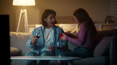 Genç evli çift evde romantik bir akşam geçiriyorlar, birlikte şarap içiyorlar, kadın kocasına hediye sunuyor.