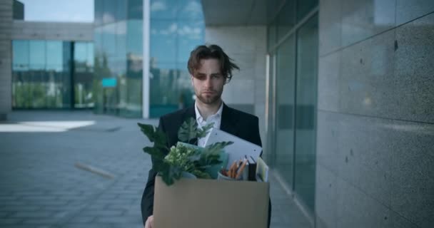 Retrato ao ar livre de deprimido demitido empregador masculino saindo do prédio de escritórios com caixa de material pessoal — Vídeo de Stock