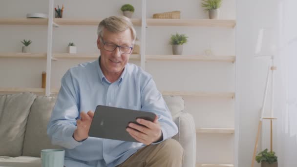 Hombre mayor alegre usando tableta digital en línea, disfrutando de Internet y gadget en casa, seguimiento de disparo, espacio vacío — Vídeos de Stock